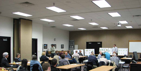 People sitting in a meeting room facing a presenter with display boards.