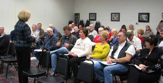 A woman addresses a seated audience in a meeting room.