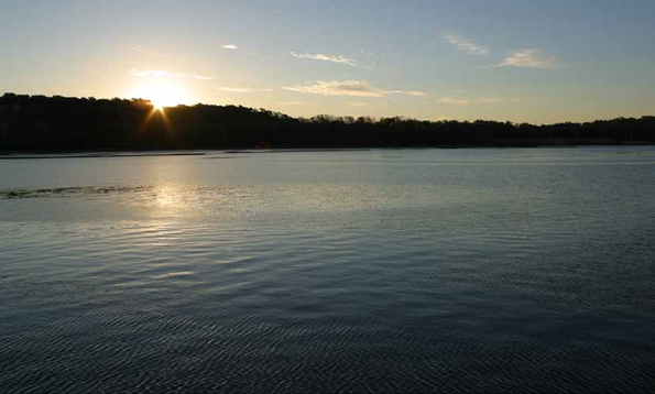 Sunset over a calm lake with distant hills.
