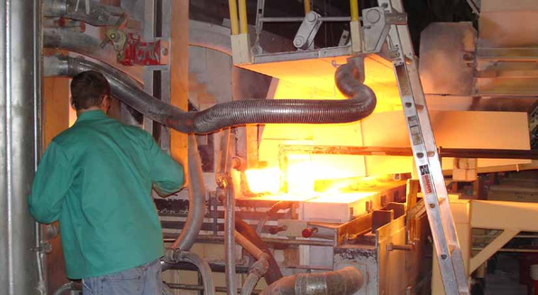 Worker in green jacket stands near a bright industrial furnace.