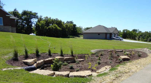 A landscaped garden bed with rocks and plants on a grassy slope.