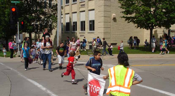 Children and adults cross a street with a school crossing guard.