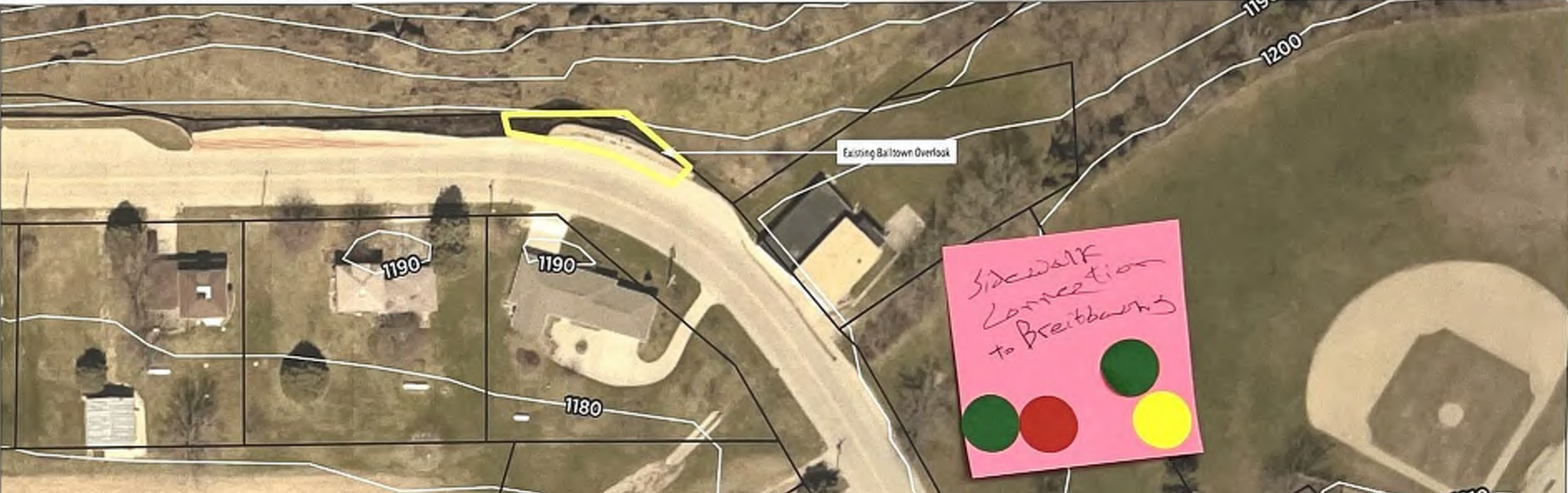 The map outlines a neighborhood along a curved road with various properties, indicated by numbered labels (1180, 1190, 1200). It includes a pink sticky note that reads 'Sidewalk connection to Breidbaut' and colored circles that may represent points of interest or priority. The layout displays how properties relate spatially to the road and surrounding areas.