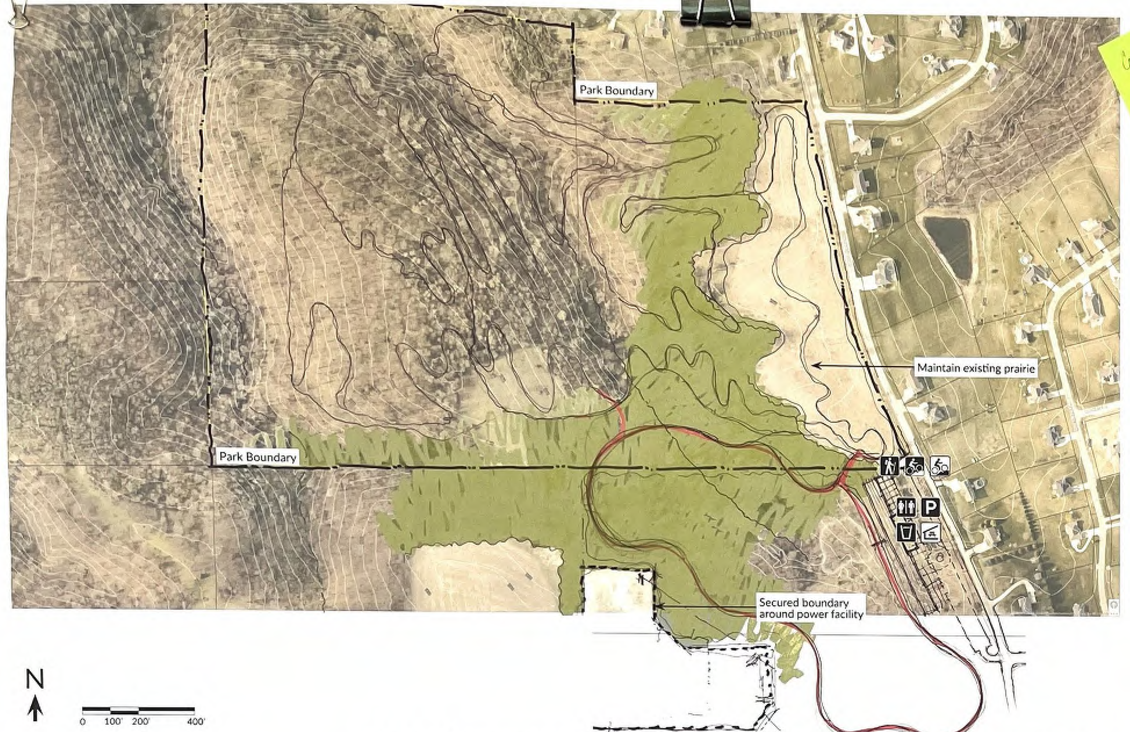 The map depicts the layout of a park with highlighted boundaries, trails for pedestrians and cyclists, and designated maintenance areas, particularly showing a secured boundary around a power facility. The visual layout indicates various routes and their relationships to the park's features, providing valuable spatial context for navigation within the area.