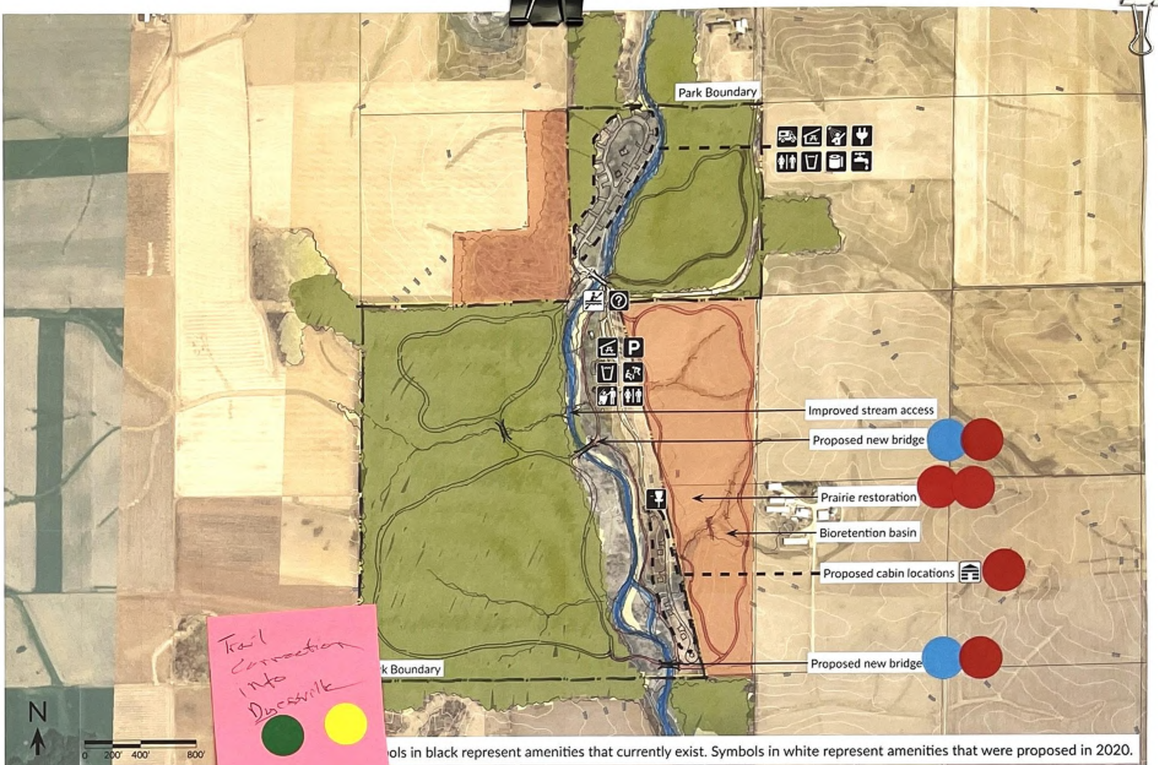 The map illustrates the layout of a park with distinct areas, including the boundary marked in green, existing amenities depicted by black symbols, and proposed developments identified with red circles. Key features are labeled, including improved stream access, prairie restoration areas, and proposed cabin locations. The map's legend describes the meaning of symbols and colors used throughout, enhancing understanding of current and future park plans.