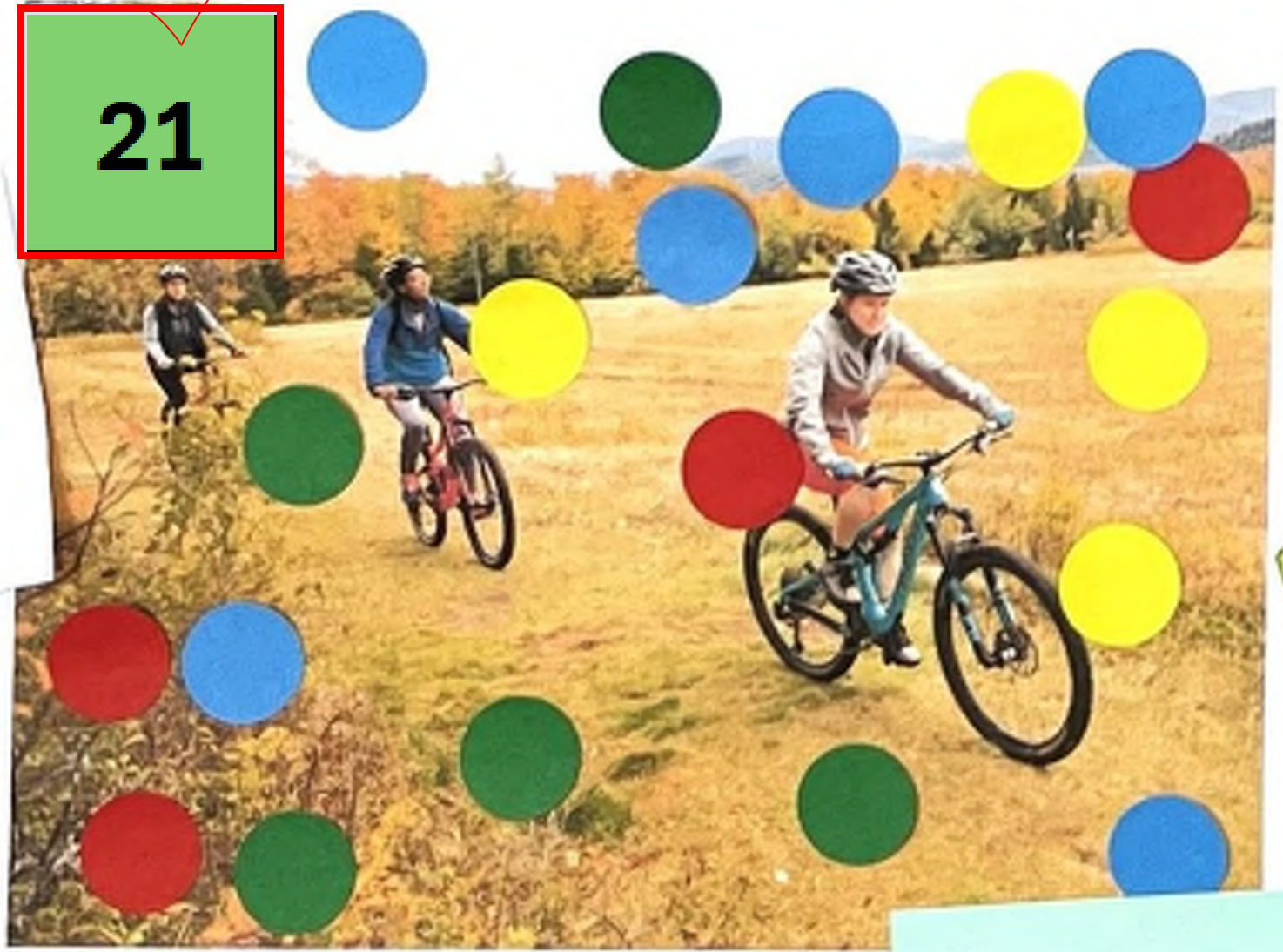 The image depicts three people riding mountain bikes through a grassy field. Two cyclists are positioned in the background, while one is in the foreground. Colorful circles in red, blue, green, and yellow overlay parts of the image, adding visual emphasis. The landscape features trees with autumn foliage, indicating a scenic outdoor setting.