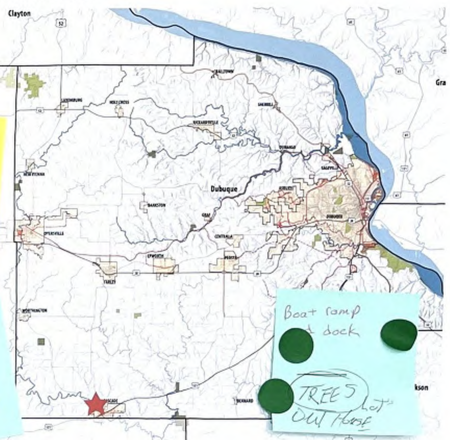 The map illustrates the Dubuque region, featuring major roads and geographical landmarks. A notable visual element is a star marker indicating a specific location in the southern part of the map. Additionally, there are annotations on sticky notes indicating 'Boat ramp & dock' and 'TREES LOT OW HOUSE.' This information helps navigate and understand the layout and significant points of interest in the area.